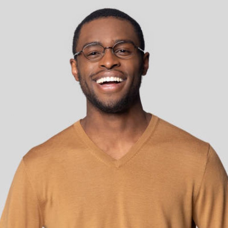 Head shot close up portrait happy smiling african american man in casual sweater looking at camera. Cheerful millennial black guy in round glasses posing for photo, isolated on grey studio background.